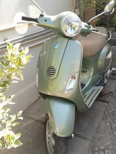 a green scooter is parked in front of a building and some plants on the sidewalk