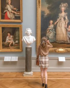 a woman standing in front of paintings and busturines on display at a museum