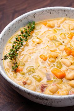 a white bowl filled with beans and carrots on top of a wooden table next to a green sprig