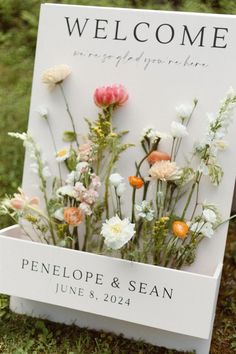 a welcome sign with flowers on it sitting in the grass