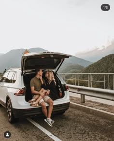 a man and woman sitting in the back of a white car on top of a mountain