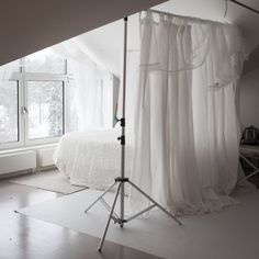 a white bed sitting in a bedroom next to a tall window on top of a hard wood floor