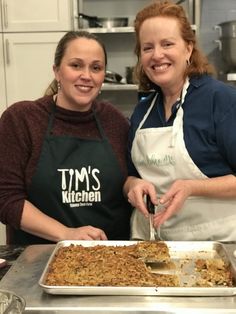 two women standing in front of a pan of food