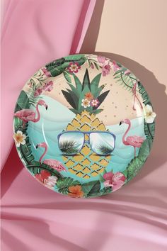 a plate with flamingos and sunglasses on it sitting on a pink cloth covered table