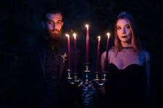 a man and woman standing next to each other with candles in front of their faces