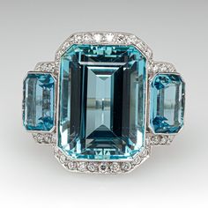 This stunning vintage cocktail ring is accented with one (1), bezel set, emerald cut natural aquamarine and flanked to each side by one (1), bezel set, emerald cut natural aquamarine. The gemstones are bordered with forty-six (46), bead set, old European cut diamonds. The shoulders of the ring are each accented with two (2), bead set, old European cut diamonds. The gemstones are bordered with milgrain edging. The ring measures 12.7mm at the top, rises 9.8mm above the finger, tapering to 2.0mm wi Elegant Emerald Cut Topaz Ring, Elegant Emerald Cut Topaz Ring With 17 Jewels, Formal Emerald Cut Topaz Ring With Gemstone Accents, Formal Emerald-cut Topaz Ring With Gemstone Accents, Emerald Cut Topaz Ring With Gemstone Accents, Emerald Cut Ring With Gemstone Accents For Formal Occasions, Formal Emerald Cut Topaz Ring With Bezel Setting, Formal Emerald-cut Topaz Ring With Bezel Setting, Platinum Topaz Ring Emerald Cut