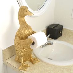 a gold duck toilet paper holder on a bathroom counter next to a sink and mirror