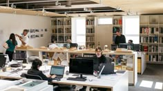 an office with people working on computers and bookshelves full of books in the background