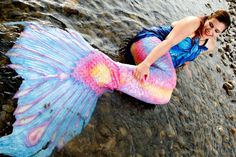 a woman is sitting in the water wearing a mermaid tail and blue shirt with pink flowers on it