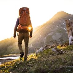 a man with a backpack walking up a hill in the mountains at sundown or sunrise