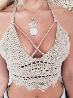 a woman wearing a crochet halter top with a silver medallion on it