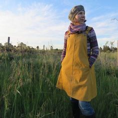 a woman standing in tall grass with her hands on her hips, wearing an apron and boots