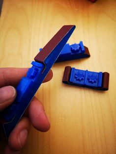 a hand holding a blue plastic object on top of a wooden table next to another piece of wood