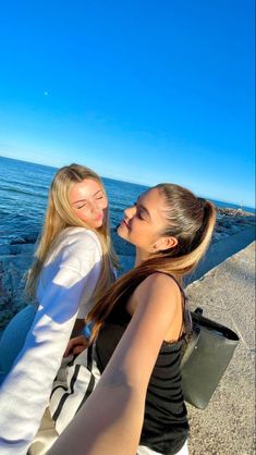 two young women standing next to each other near the ocean