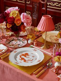 the table is set with pink and yellow flowers in vases, plates, silverware, and gold cutlery