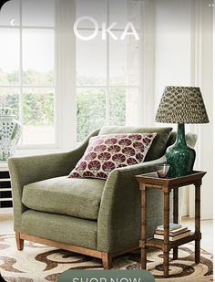 a green chair sitting in front of a window next to a table with a lamp on it