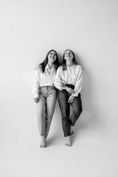 two women sitting next to each other in front of a white wall