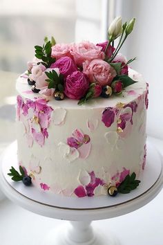 a white cake with pink and purple flowers on it sitting in front of a window