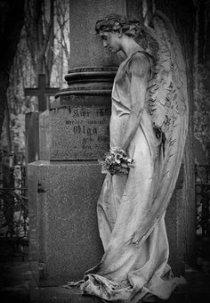 black and white photograph of an angel standing in front of a grave with flowers on it