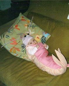 a baby laying on top of a green couch next to a stuffed animal and pillows