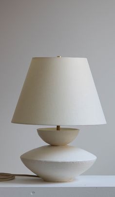 a white lamp sitting on top of a table next to a light switch and plugged in