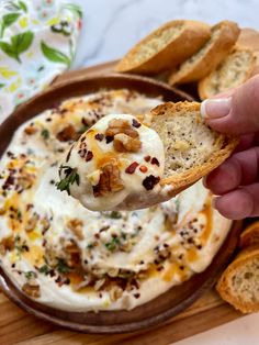 a hand holding a piece of bread over a bowl of dip with crackers on the side