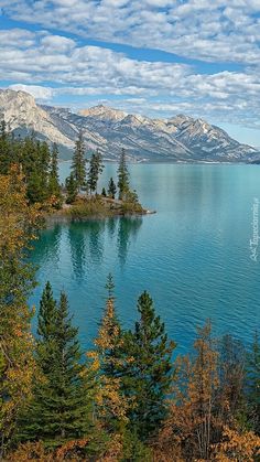 a lake surrounded by trees and mountains under a cloudy blue sky with white puffy clouds