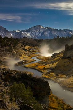 a river running through a valley surrounded by mountains under a night sky filled with stars