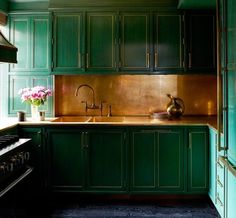 a kitchen with green cabinets and an oven in the center, along with a vase of flowers on the counter