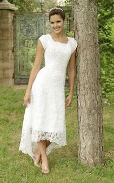 a woman standing next to a tree wearing a white dress