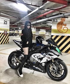 a woman sitting on top of a motorcycle in a parking garage next to a sign