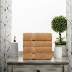 towels stacked on top of a dresser next to a potted plant