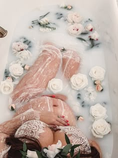 a woman laying down in a bathtub with flowers on the side and petals all over her body