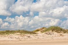 a man riding a surfboard on top of a sandy beach under a cloudy blue sky