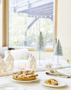 a table topped with white plates filled with food and desserts next to a window