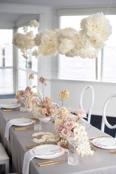 the table is set with white and pink flowers in vases, plates and silverware