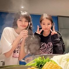 two girls are making peace signs with their hands in front of a bowl of food