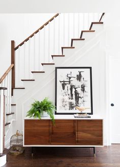 a wooden cabinet under a stair case next to a plant on top of a table