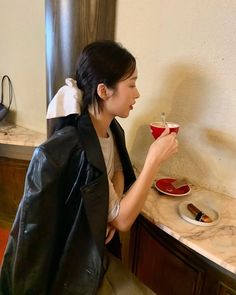 a woman sitting at a counter drinking out of a cup with a spoon in her hand