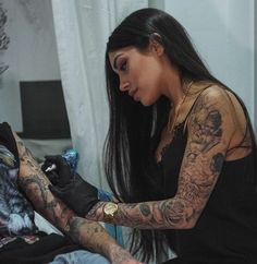 a woman with tattoos on her arm is sitting next to a man in a black shirt