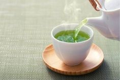 a white teapot pouring green tea into a cup on top of a saucer