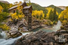 a wooden cabin sitting on top of a rocky hillside next to a river and forest