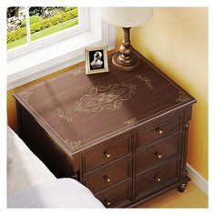 a wooden desk with an ornate design painted on the top and bottom, in front of a window