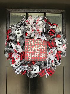 a red and black christmas wreath on a front door with the words merry christmas y'all