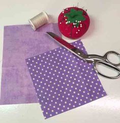 scissors, thread and fabric sitting on top of a white table with purple polka dot paper