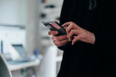 a person holding a cell phone in their hand while standing next to a computer desk