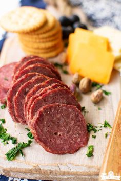 sliced salami on a cutting board next to crackers and cheese