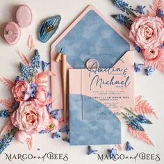 the wedding stationery is laid out on top of each other, with pink flowers and blue envelopes