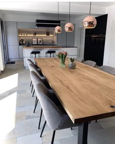 a large wooden table surrounded by grey chairs and vases with flowers on it in a modern kitchen