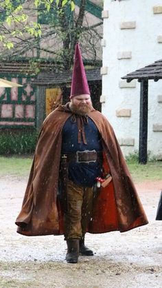 a man dressed up as a gnome with a cape and boots on walking in the rain